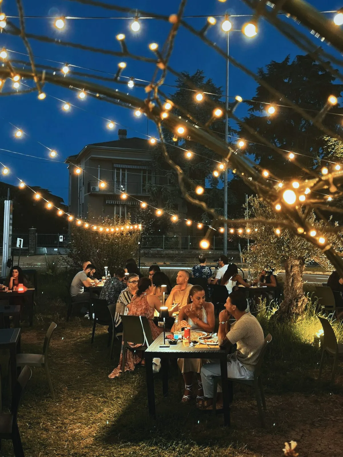 Il giardino di Cittadella Parma in Via Paradigna la sera, con le luci accese e i tavoli occupati