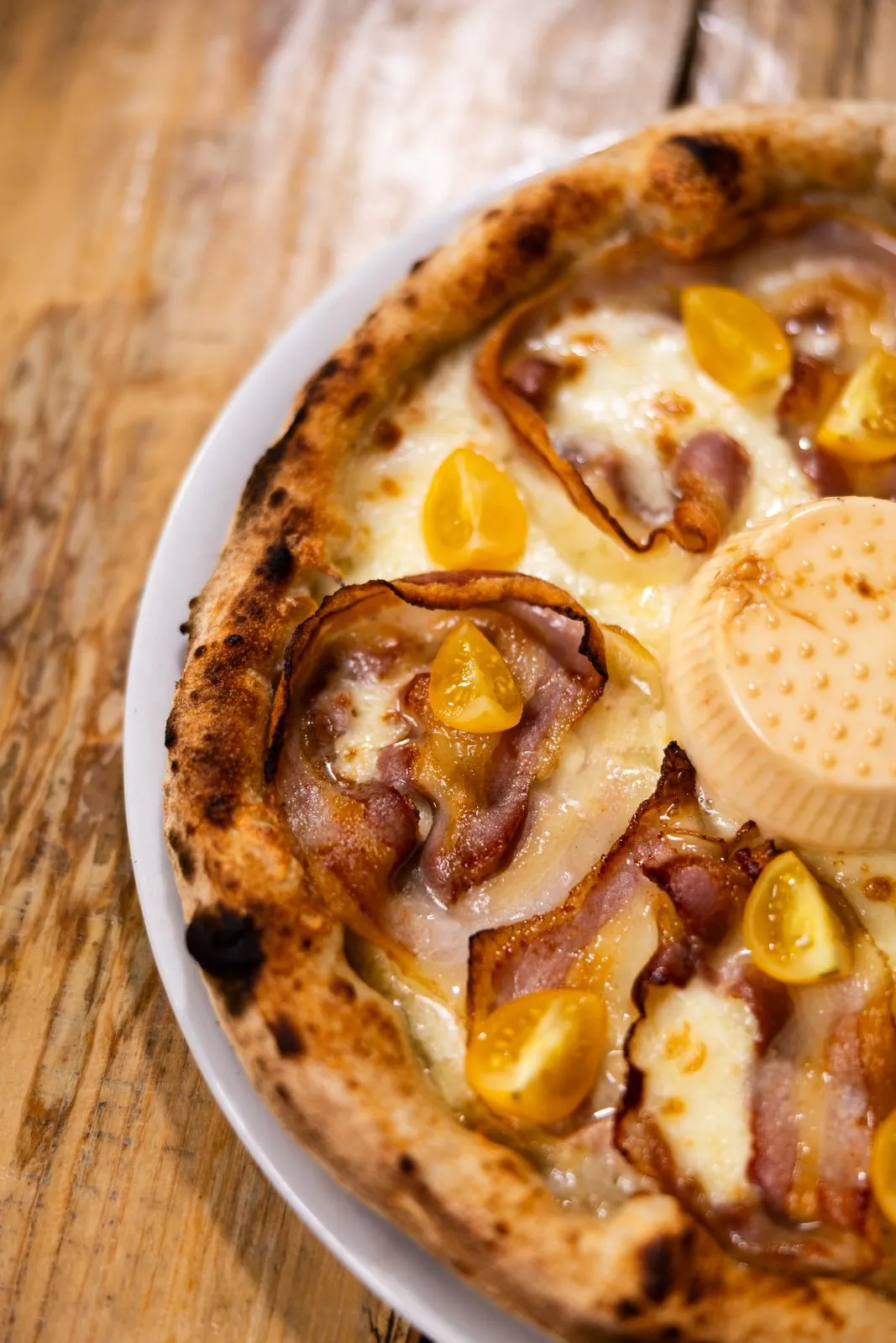 Primo piano di una pizza Cittadella Parma con pancetta croccante, pomodorini gialli e un formaggio fresco al centro
